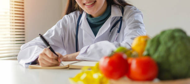 banner panorâmico. jovem nutricionista médica ou médica sorrindo e escrevendo plano de dieta e vegetais frescos, frutas na mesa no escritório, nutrição, estilo de vida saudável, alimentação saudável, conceito de dieta - dietology - fotografias e filmes do acervo