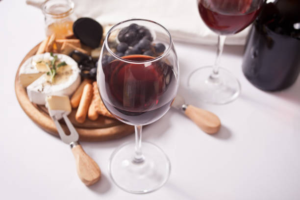 Two glass of red wine and plate with assorted cheese, fruit and other snacks for party stock photo
