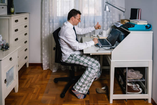 Man teleworking wearing shirt, tie and pajama pants Man working from home with laptop wearing shirt, tie and pajama pants desk lamp photos stock pictures, royalty-free photos & images