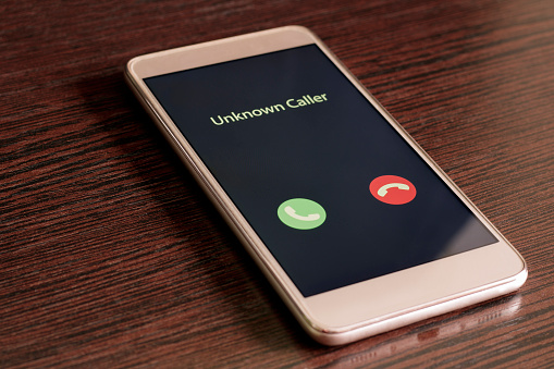 Unknown caller. White smartphone with incoming call from an unknown number on a wood table background. Incognito or anonymous