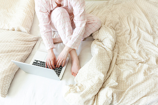 Mobile Office at home. Young woman in pajamas sitting on bed at home working using on laptop pc computer. Lifestyle girl studying indoors. Freelance business quarantine concept