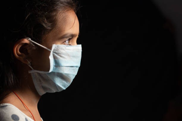 joven adolescente con máscara facial médica en cuarto oscuro en la cuarentena de casa debido a la covid 19 o brote de coronavirus - concepto de esperanza y lucha para poner fin a la crisis del virus. - isolated despair hope assistance fotografías e imágenes de stock