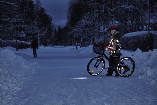 fille sur un vélo dans une soirée d’hiver. la lumière est réfléchie par les réflecteurs de vêtements et les roues de vélo. cyclisme sûr dans le temps sombre. - road reflector photos et images de collection