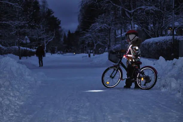 Photo of Girl on a bicycle in a winter evening. Light is reflected from clothing reflectors and bicycle wheels. Safe cycling in the dark time.