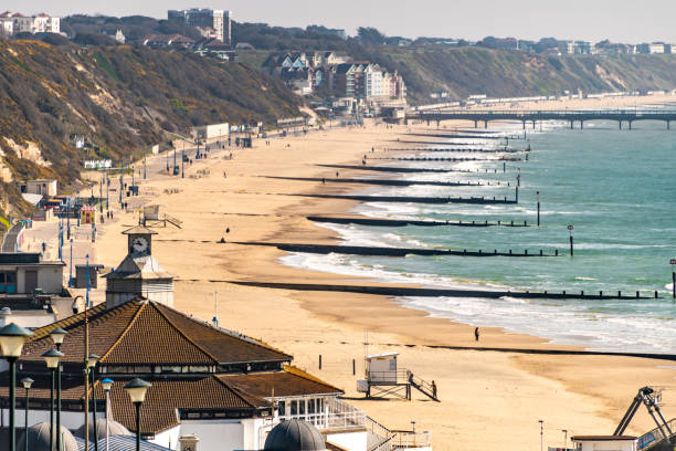 Long shot of Bournemouth Beach with groynes Bournemouth, UK. March 24 2020. Long shot of Bournemouth Beach with groynes, people walking on the seafront. boscombe photos stock pictures, royalty-free photos & images