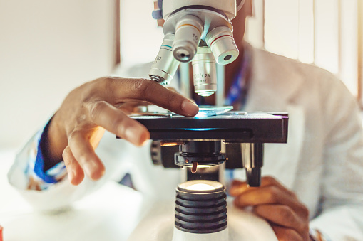 African-American men in a laboratory microscope with microscope slide in hand.