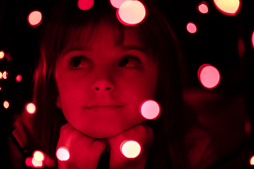 Little girl dreaming in the dark with red boke Christmas light