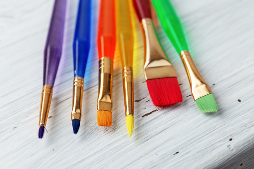 Colorful paint brushes - blue, orange, yellow, red, green, violet on wooden table. Concept creativity education