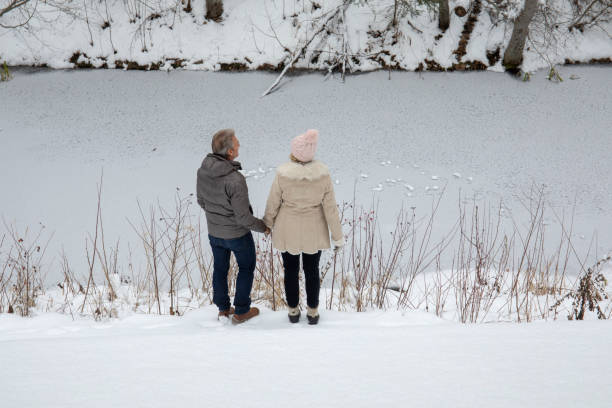 istock Mature couple walk through snow toward river 1214748068