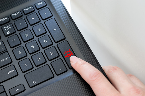 Keyboard corner of a black laptop with a female finger clicking on a fake news button. The concept of spreading false news, messages on the Internet