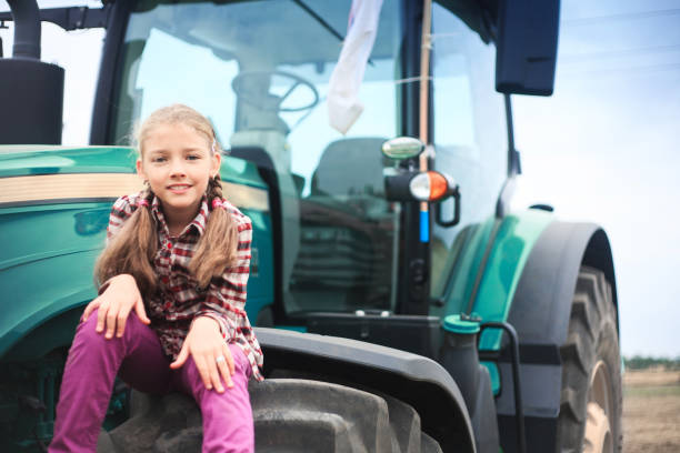 Chica linda cerca del tractor moderno en el campo. El concepto de trabajo de campo. - foto de stock