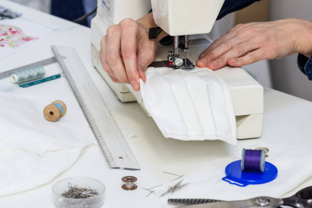 Seamstress is sewing a  face mask of white material
