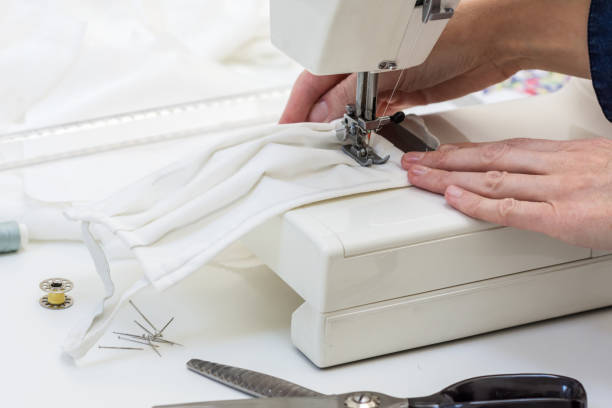 istock Seamstress is sewing a  face mask of white material 1214751778