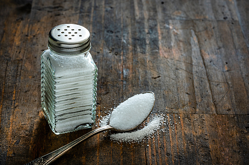 Slightly above and close view of a fallen glass saltshaker spilling salt in a wooden plate.