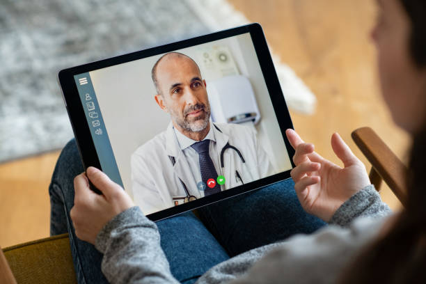 Patient doctor online consultation Back view of young woman making video call with her doctor while staying at home. Close up of patient sitting on armchair video conferencing with general practitioner on digital tablet. Sick girl in online consultation with a mature physician. telemedicine stock pictures, royalty-free photos & images