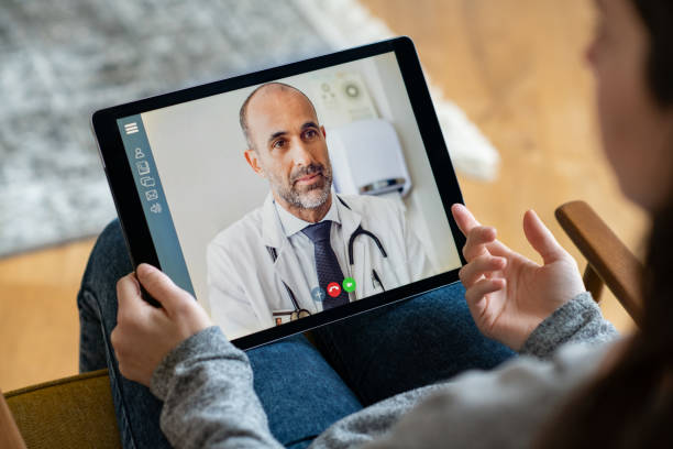 Patient doctor online consultation Back view of young woman making video call with her doctor while staying at home. Close up of patient sitting on armchair video conferencing with general practitioner on digital tablet. Sick girl in online consultation with a mature physician. Distant stock pictures, royalty-free photos & images