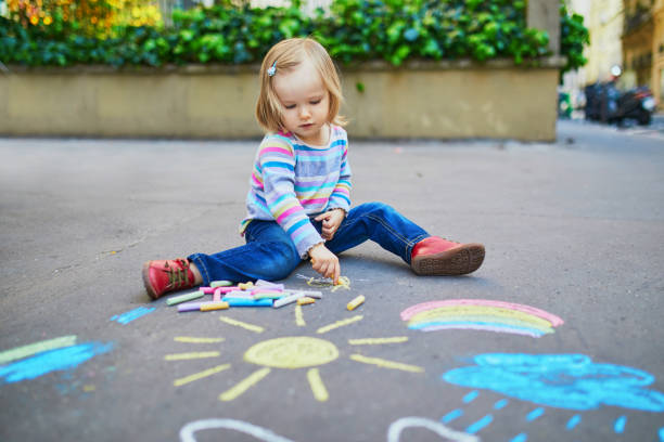 adorabile bambina che disegna con gessetti colorati sull'asfalto - little girls sidewalk child chalk foto e immagini stock
