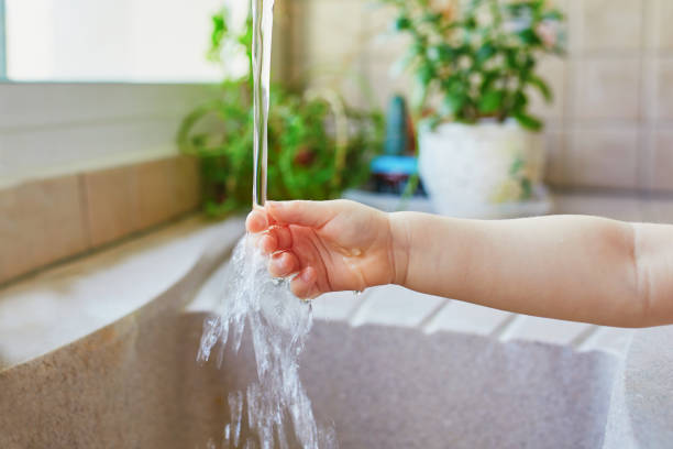 Toddler girl washing her hands under kitchen sink. Little child having fun with water. Hygiene and skin care for kids