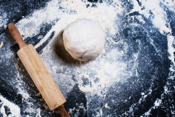 istock Preparation of the dough. Top view. Pizza dough and rolling pin on black table. 1214754132