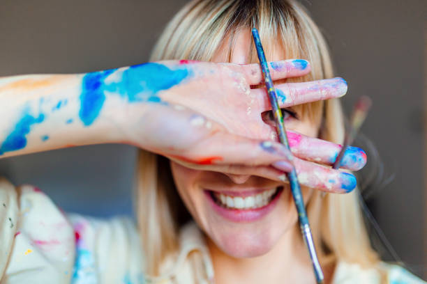 Portrait of a young blonde artist Portrait of a beautiful young blonde woman covered in colors, covering her face and holding a paintbrush fine art painting photos stock pictures, royalty-free photos & images