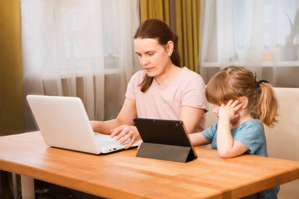 istock Home office. Working from home vs. Mom with two kids Work on the Internet on a laptop and kid study online at home.  quarantine. Corona Virus. 1214755291