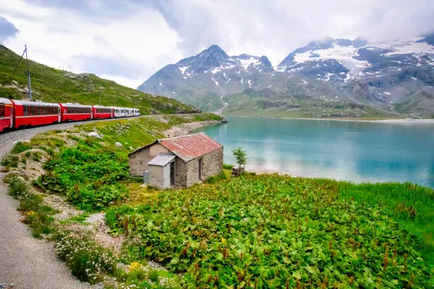 The Swiss train Bernina Express travels through the Alps, in the background snow-capped mountains.