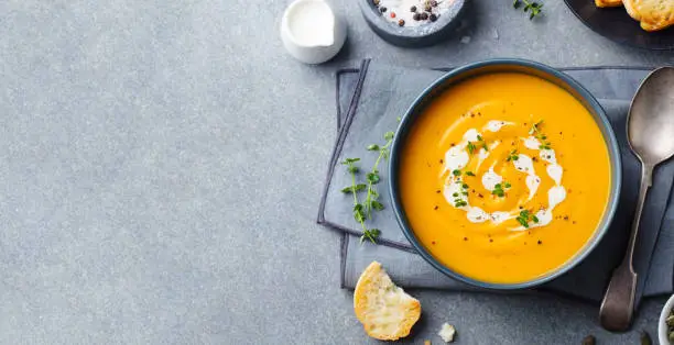 Photo of Pumpkin, carrot cream soup in a bowl. Grey background. Top view. Copy space.