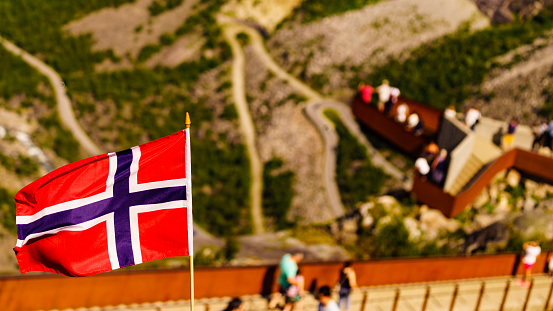 Trollstigen mountain road landscape in Norway, Europe. Norwegian flag waving and many tourists people on viewing platform in background. National tourist route.
