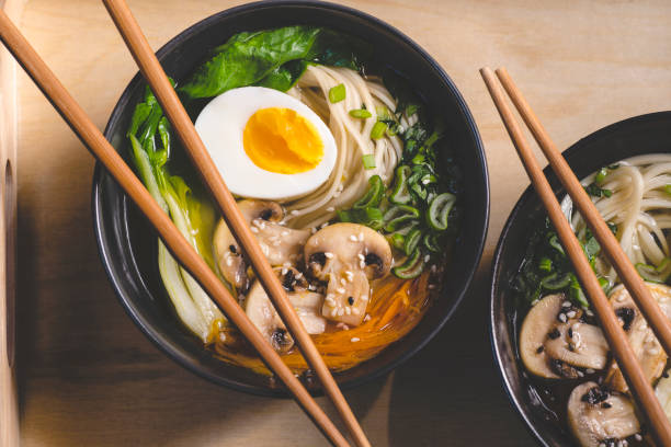 traditionelle japanische ramensuppe mit pilzen, bok choy, grüns in zwei schwarzen schalen auf dem orangen hintergrund, ansicht von oben, nahaufnahme - chinesischer senfkohl stock-fotos und bilder