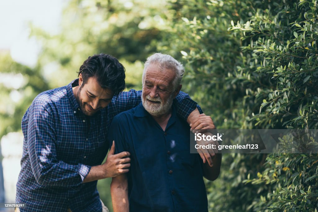Der alte Mann und sein Sohn gehen im Park spazieren. Ein Mann umarmt seinen älteren Vater. Sie sind glücklich und lächelnd - Lizenzfrei Vater Stock-Foto