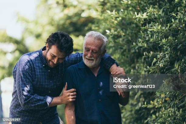 The Old Man And His Son Are Walking In The Park A Man Hugs His Elderly Father They Are Happy And Smiling Stock Photo - Download Image Now