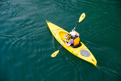 In Austin, United States a man paddles a yellow kayak on the Colorado River on a sunny spring day.
