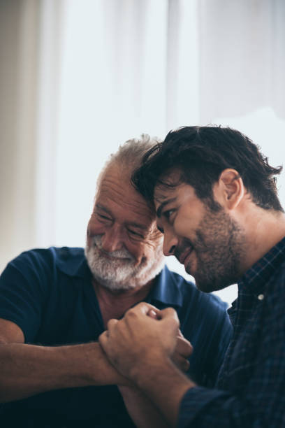 An adult hipster son and senior father at home, talking. stock photo