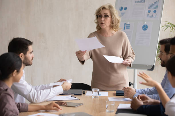 istock Female presenter share handouts at team office meeting 1214766096