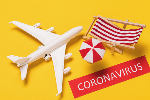 Toy plane, note with text and beach accessories on yellow background, view from above. The concept of cancellation by leave due to the outbreak of coronavirus COVID-19