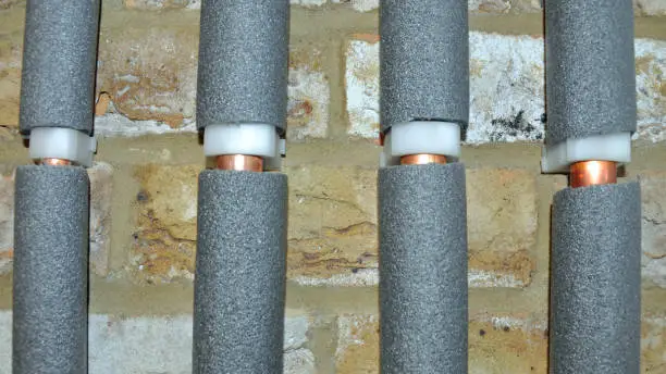 Four copper water pipes in grey foam insulation against an interior brick wall. Billericay, Essex, United Kingdom, March 25, 2020