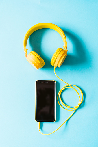 top view of yellow headset and mobile phone over blue background. Modern technology concept