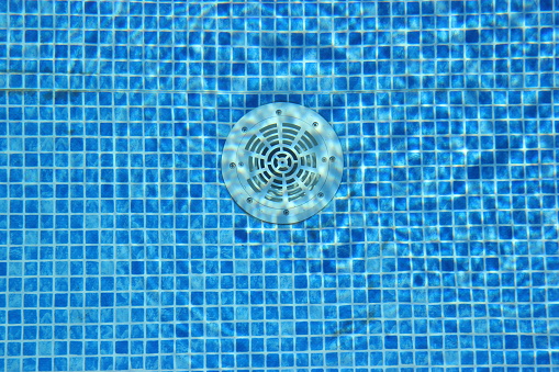Drain hole in the pool with blue tile. Clean water.