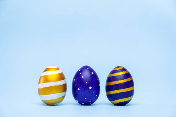 istock Three easter trendy colored classic blue and golden decorated eggs striped pattern on blue. Happy Easter card with copy space for text. Minimal style 1214776579