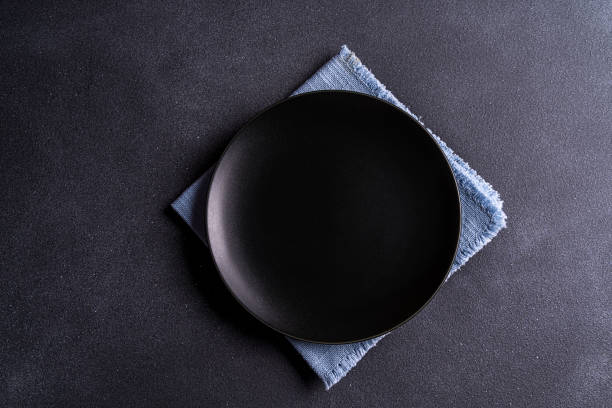 istock Empty black plate over napkin on black table top view, copy space for text. 1214779991