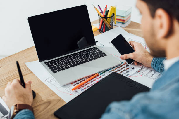 istock Selective focus of ux designer using smartphone near laptop, graphics tablet and layouts with sketches on table on grey background 1214784483