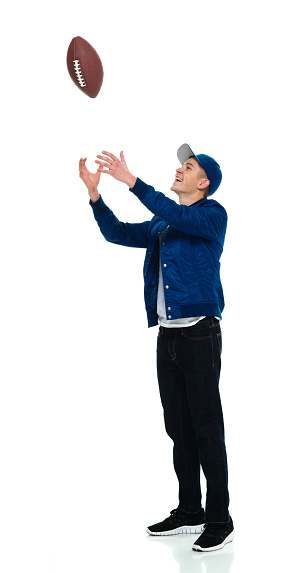 Side view of aged 18-19 years old caucasian young male standing in front of white background wearing sports shoe who is smiling who is throwing