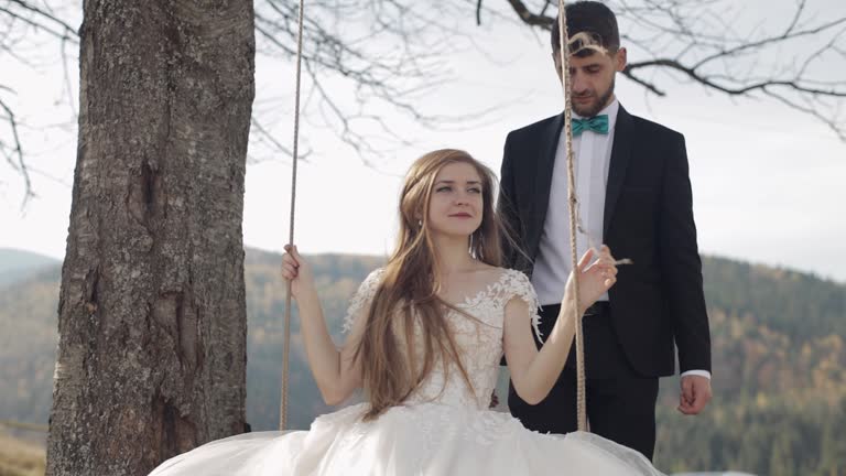 Newlyweds. Caucasian groom with bride ride a rope swing on a mountain slope