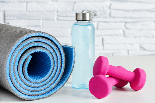 Pink dumbbells, bottle of isotonic drink and fitness mat on white wooden table. Healthy lifestyle concept. Sports.