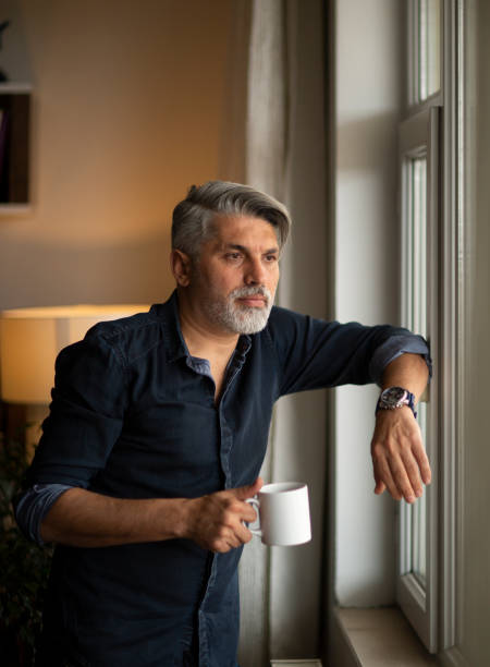 istock Thoughtful businessman with cup at window sill 1214794483