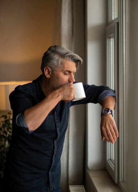 istock Thoughtful businessman with cup at window sill 1214794694