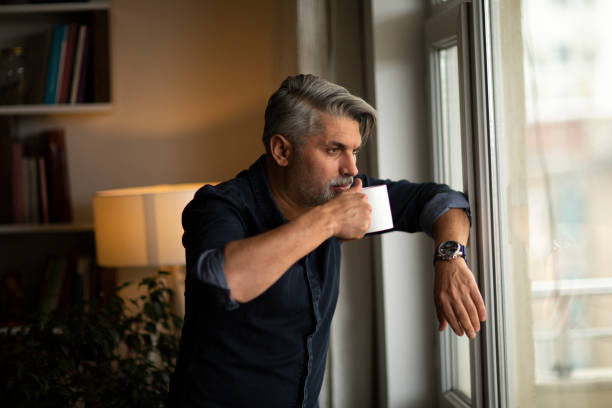 istock Thoughtful businessman with cup at window sill 1214794909