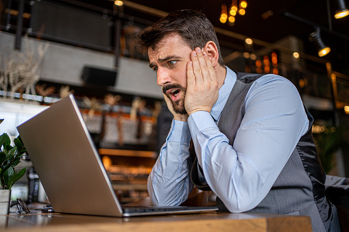 Worried businessman looking at his laptop after reading a bad news on a e-mail at the coffee shop