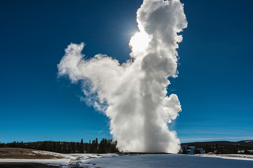 Old Faithful Geyser in the Upper Geyser Basin of Yellowstone National Park in the winter with steam. Sun.