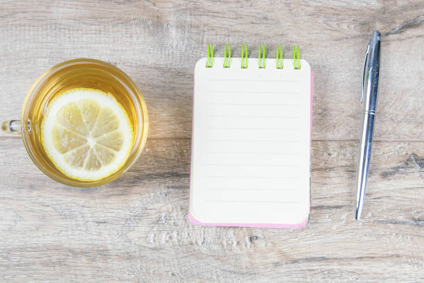 istock An open notebook on a wooden table, next to stand a silver pen and a cup of mint tea with lemon 1214803152